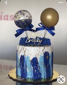 a blue and white birthday cake with gold balloons on the top that says happy birthday