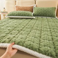 a bed with green bedspread and two pillows on top of the headboard