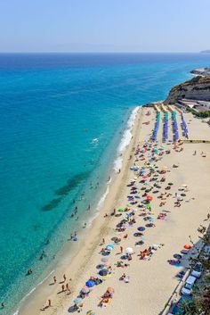 a beach with many people and umbrellas on the sand next to the blue water