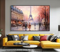 a living room with a yellow couch and large painting on the wall above it that has people walking down the street in front of the eiffel tower