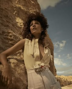 a woman standing next to a large rock wearing a white shirt and skirt with flowers on it