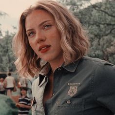 a woman with blonde hair wearing a green shirt and looking off into the distance while standing in front of a group of people