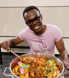 a man in pink shirt holding a large pot filled with food and smiling at the camera