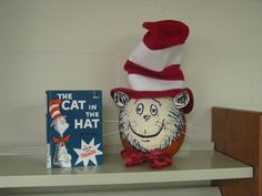 the cat in the hat is next to a book and a stuffed animal on a shelf