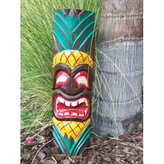 a tiki mask sitting next to a tree in front of some grass and flowers