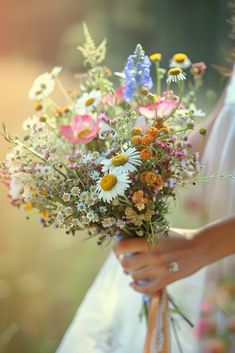 a bride holding a bouquet of wildflowers and daisies