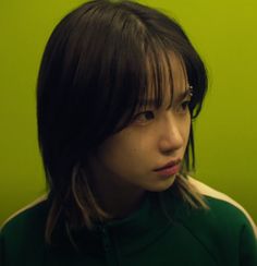 a young woman with bangs standing in front of a green wall