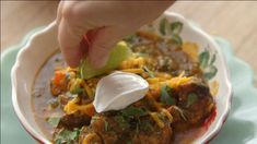 a person dipping sour cream on top of some taco meat in a white bowl