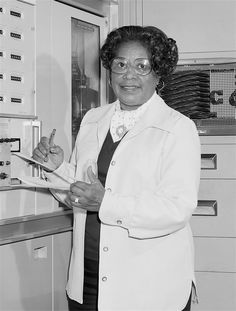 an older woman in glasses is holding a clipboard and looking at the camera while standing next to some drawers