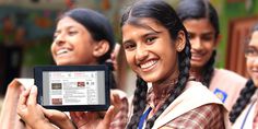 three girls are smiling and holding up a tablet