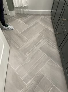 a person standing on the bathroom floor next to a bathtub and sink with grey tile