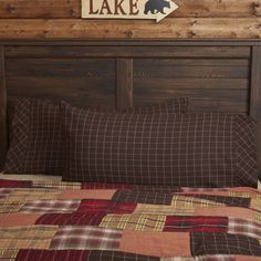 a bed with a plaid comforter and wooden headboard, along with a bear sign on the wall