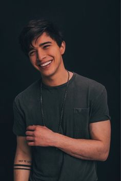 a young man with tattoos on his arm and chest smiles at the camera while wearing a black t - shirt