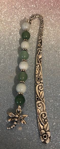 a silver necklace with green beads and a dragon broochel on the end is laying next to it