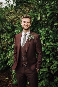 a man wearing a suit and tie standing in front of some bushes with a boutonniere on his lapel