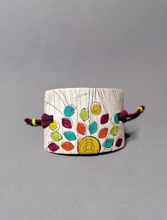 a white bracelet with multicolored beads and tassels on the end, sitting on a gray surface