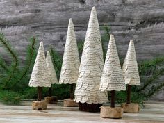 four paper christmas trees sitting on top of a wooden table next to pine cones and branches