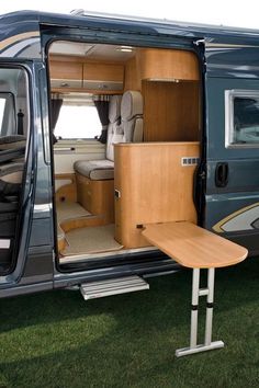 the interior of an rv parked on grass with its door open and table attached to it