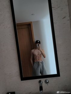 a shirtless man taking a selfie in front of a mirror with his hat on