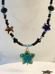 16 inch beaded star necklace arrives in ready to gift packaging. Black and pale blue seed beads interspersed with small electroplated stars and an aqua-green carnival glass star come together for a  whimsical choker necklace. Fairy core aesthetic is perfect for a young girl or teen's birthday or for anyone who loves sparkly celestial themed jewelry. Clasp and fittings are sterling silver. Adjustable Celestial Necklace With Star Charm, Adjustable Star-shaped Magical Jewelry, Adjustable Star Charm Festival Jewelry, Star Charm Necklace For Festivals, Adjustable Star Charm Jewelry For Festivals, Star-shaped Beaded Necklaces For Festivals, Celestial Star Jewelry For Festival, Star Charm Necklaces With Round Beads For Jewelry Making, Adjustable Turquoise Jewelry With Star Charm