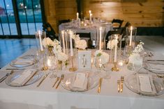 the table is set with silverware and white flowers in vases, candles, and menu cards