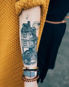 a woman with a tattoo on her arm holding onto a bracelet that has an image of a house on it