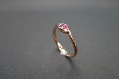 This brilliant classic engagement ring is set in 14K white gold. The center stone, a 3mm round brilliant cut ruby is set in a four prong setting with two brilliant cut round diamonds. Product Specifications: - 3mm natural Ruby at the center - 2 Round Brilliant cut Diamonds, total carat around 0.03ct - D-F in color and VS with Heart and Arrow (Ideal cut) - 14K Rose gold - Ring Width: 2.20mm Currently made to order pieces may take up to 10-15 business days to complete, or let me know if you need i Modern Round Cut Ruby Ring For Wedding, Modern Round Cut Ruby Wedding Ring, Wedding Rings With Pink Sapphire In Bezel Setting, Wedding Pink Sapphire Ring With Bezel Setting, Elegant Rose Gold Stackable Rings With Pink Sapphire, Elegant Ruby Ring With Tension Setting, Elegant Promise Ruby Ring With Bezel Setting, Modern Ruby Rings For Wedding, Minimalist Oval Ruby Wedding Ring