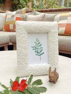 a white frame with a green leaf on it next to a small rabbit figurine