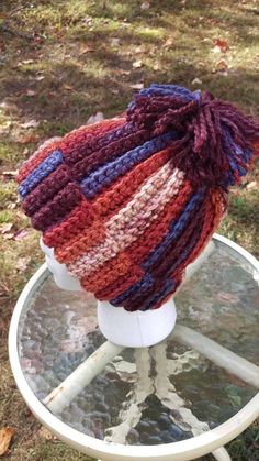 a knitted hat sitting on top of a white stand in the grass next to a tree