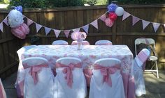 a table covered in pink and white cloths next to a fence with bunting