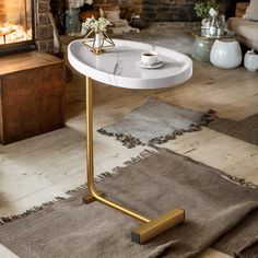 a white table with gold legs and a candle holder on the end, in front of a fireplace