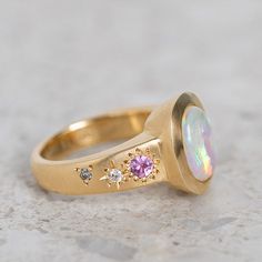 Our Sun Punch Ring has been set with a Crystal Opal from Coober Pedy and bead set with Pink Sapphires, G/VS White Diamonds and Salt & Pepper Diamonds in the band. Opal measures approx. 10 x 8mm. There are a total of three birlliant cut pink sapphires and four brilliant cut diamonds. Band width tapers from approx. 6mm to 3.4mm at the back of the band. Gold weight approx. 11g in 14ct, 12.6g in 18ct. This ring is pictured with a matte finish. For a polished finish please leave a note at the checkout. Please note, we will match the opal as close to the image as possible. Each opal is unique and may vary in appearance and colour from what is depicted on the site. Opal Signet Ring, Sarah Gardner, Pink Rings, Cosmic Ring, Pink Opal Ring, Coober Pedy, Crystal Opal, Bead Set, Put A Ring On It