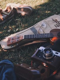 a guitar, camera and shoes laying on the ground in the grass near someone's feet