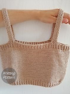 a hand holding a knitted bag on top of a white table