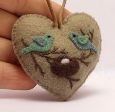 a hand holding a heart shaped ornament with two birds on it