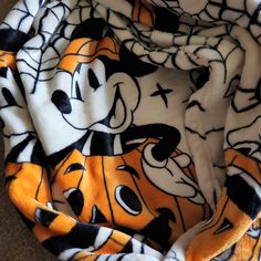 an orange and black mickey mouse print blanket on the floor with it's hood pulled up