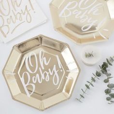 gold foil plates with the words oh baby printed on them next to flowers and greenery