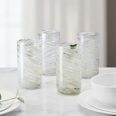 three clear vases sitting on top of a white table next to plates and cups