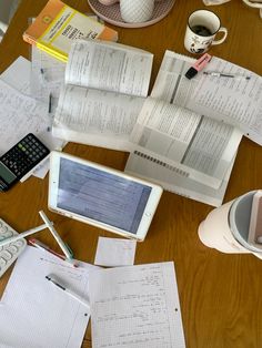 a wooden table topped with lots of papers and laptop computer sitting on top of it