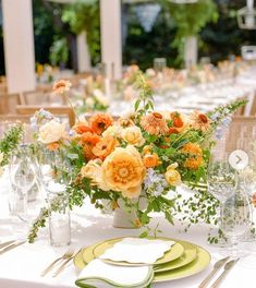 an arrangement of flowers and greenery on a table set for a formal dinner or party