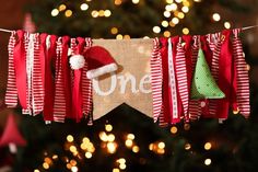 a christmas banner hanging from a string with one written on it and two small trees in the background