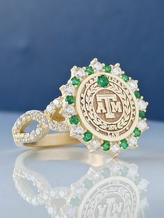 a gold ring with green and white stones in the center on a reflective surface against a blue background