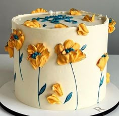 a cake decorated with yellow flowers and blue leaves on a white platter, ready to be eaten