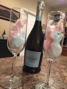 two wine glasses filled with pink and blue cotton floss next to a bottle of champagne