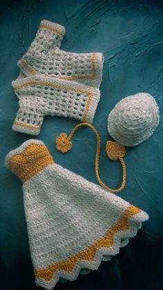 a crocheted baby outfit and hat on a blue surface next to a ball