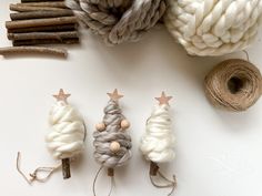 three small knitted christmas trees next to twine and balls of yarn on a white surface