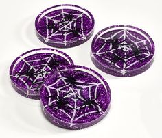 three purple and white coasters with black spider web designs on the front, one in the middle