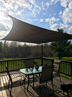 an outdoor table and chairs on a deck with a shade over it's head