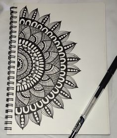 a spiral notebook with black and white doodles on it, next to a pen