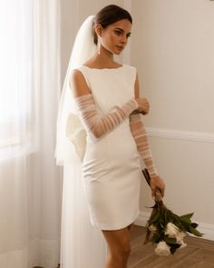 a woman in a white wedding dress holding a bouquet and wearing an arm length veil